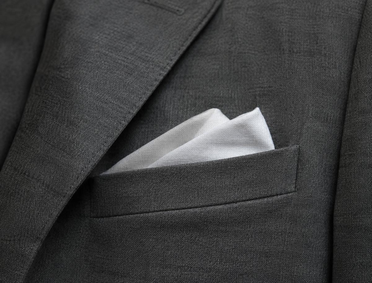Close-up of a welted breast pocket with a white linen pocket square on a grey suit jacket